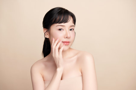 A beautiful young Asian woman with clean, fresh skin against a beige background. Skincare, facial treatment, cosmetology, beauty, and spa. An elegant portrait of an Asian woman.の写真素材