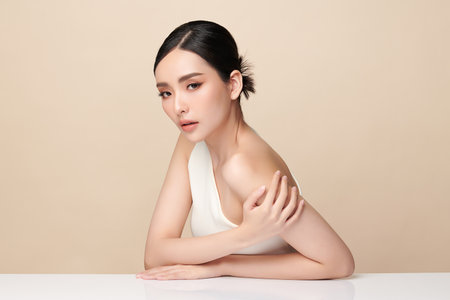 A beautiful young Asian woman with clean, fresh skin against a beige background. Skincare, facial treatment, cosmetology, beauty, and spa. An elegant portrait of an Asian woman.の写真素材