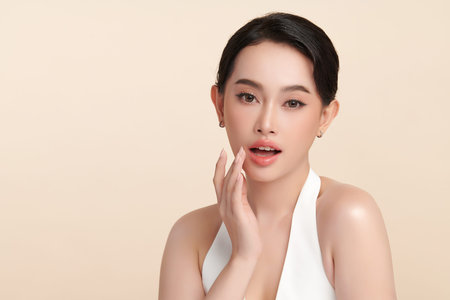 A beautiful young Asian woman with clean, fresh skin against a beige background. Skincare, facial treatment, cosmetology, beauty, and spa. An elegant portrait of an Asian woman.の写真素材