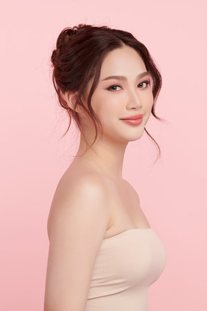 A beautiful young Asian woman with clean, fresh skin against a pink background. Skincare, facial treatment, cosmetology, beauty, and spa. An elegant portrait of an Asian woman.の写真素材