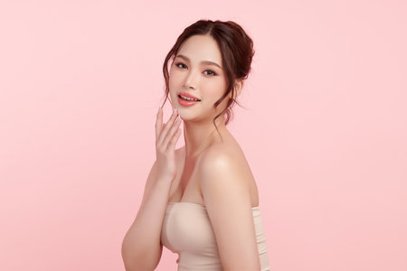 A beautiful young Asian woman with clean, fresh skin against a pink background. Skincare, facial treatment, cosmetology, beauty, and spa. An elegant portrait of an Asian woman.の写真素材