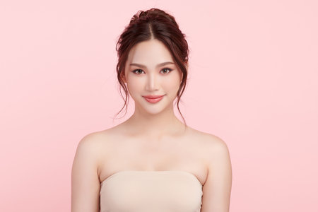 A beautiful young Asian woman with clean, fresh skin against a pink background. Skincare, facial treatment, cosmetology, beauty, and spa. An elegant portrait of an Asian woman.の写真素材