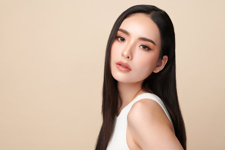 A beautiful young Asian woman with clean, fresh skin against a beige background. Skincare, facial treatment, cosmetology, beauty, and spa. An elegant portrait of an Asian woman.の写真素材