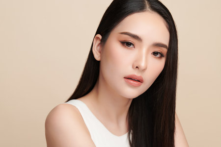 A beautiful young Asian woman with clean, fresh skin against a beige background. Skincare, facial treatment, cosmetology, beauty, and spa. An elegant portrait of an Asian woman.の写真素材