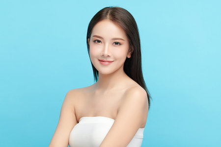 A beautiful young Asian woman with clean, fresh skin against a blue background. Skincare, facial treatment, cosmetology, beauty, and spa. An elegant portrait of an Asian woman.の写真素材
