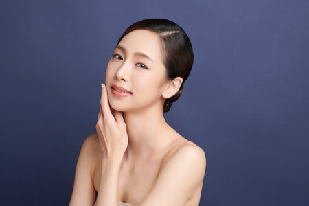 A beautiful young Asian woman with clean, fresh skin against a blue background. Skincare, facial treatment, cosmetology, beauty, and spa. An elegant portrait of an Asian woman.の写真素材