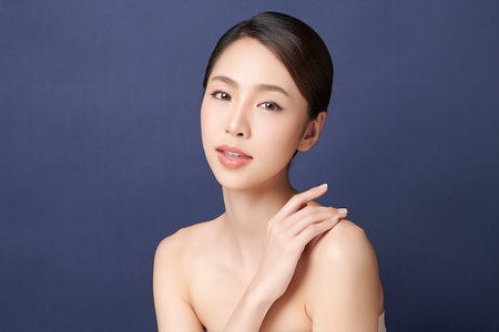 A beautiful young Asian woman with clean, fresh skin against a blue background. Skincare, facial treatment, cosmetology, beauty, and spa. An elegant portrait of an Asian woman.の写真素材