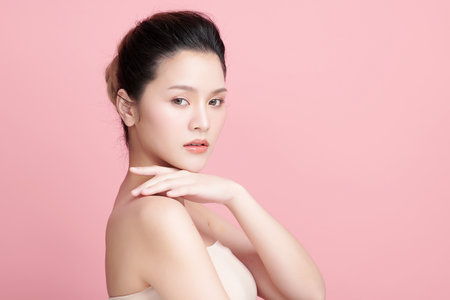 A beautiful young Asian woman with clean, fresh skin against a pink background. Skincare, facial treatment, cosmetology, beauty, and spa. An elegant portrait of an Asian woman.の写真素材