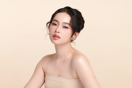 A beautiful young Asian woman with clean, fresh skin against a beige background. Skincare, facial treatment, cosmetology, beauty, and spa. An elegant portrait of an Asian woman.の写真素材