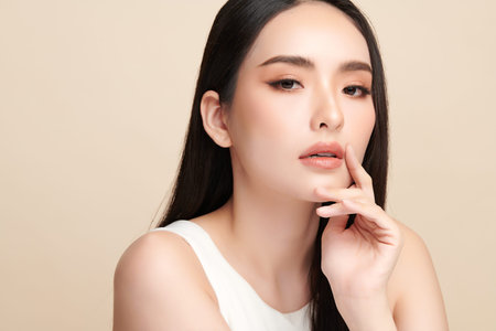 A beautiful young Asian woman with clean, fresh skin against a beige background. Skincare, facial treatment, cosmetology, beauty, and spa. An elegant portrait of an Asian woman.の写真素材