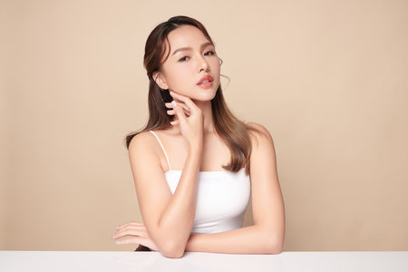 A beautiful young Asian woman with clean, fresh skin against a beige background. Skincare, facial treatment, cosmetology, beauty, and spa. An elegant portrait of an Asian woman.の写真素材