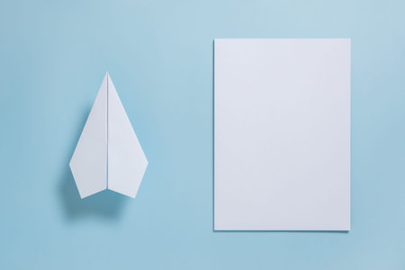 Flat lay of white paper plane and blank paper on pastel blue color backgroundの写真素材