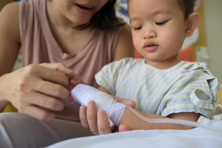 mother holding child's hand receiving iv saline solution in hospital.の写真素材