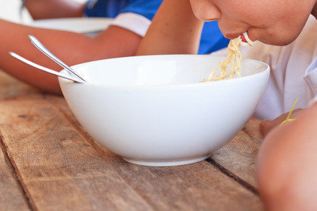 Children eating their  instant noodle in white bowl on wood table,Focused on Left hand of first person.の写真素材