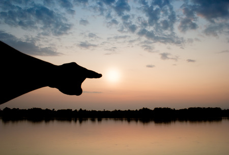 silhouette hand point to the sun in sun set.の写真素材
