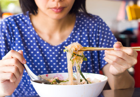Asian women use chopstick eating delicious noodle in white bowl ,Focused on noodle.