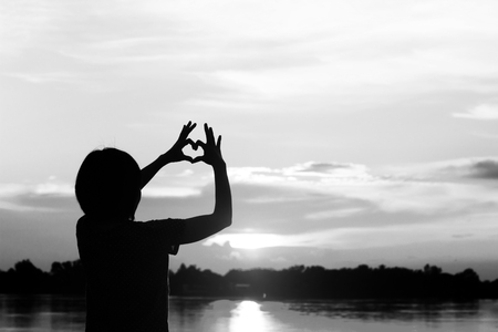 silhouette women use her hand make heart form with sun set.の写真素材