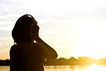 Silhouette of woman listening song over beautiful sunset background.の写真素材