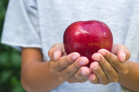 Asian boy hand holding red apple  on green natural background.の写真素材