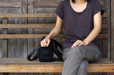 Asian woman waiting siting on wooden chair with wall background.の写真素材