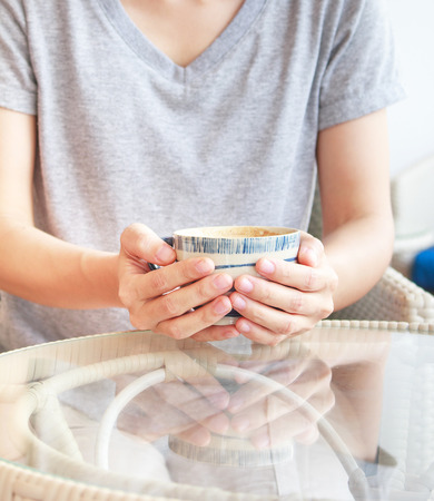 Asian woman is holding a cup of hot coffee on glass table.Focused at hand.の写真素材