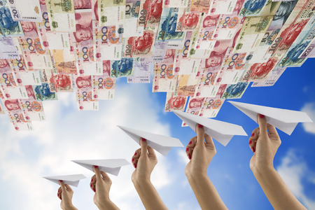 Hand holding paper plane under China money bills flyingの写真素材