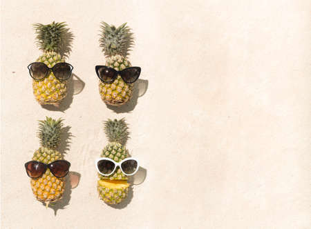 Pineapples wearing sunglasses on sand backgroundの写真素材