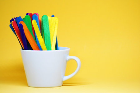 Colorful Ice cream stick on the white cup isolated with yellow pastel background -  Decorate Back to school concept with copy spaceの写真素材