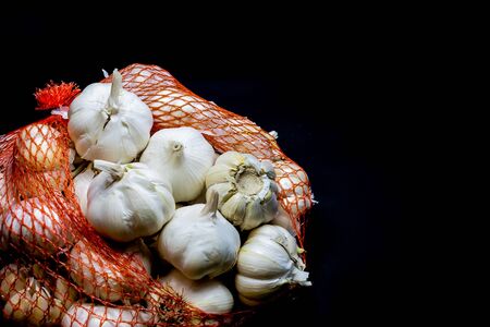 Garlic cloves and bulbs in string bag. Isolated on black background . White onions of garlic in net sack bought in greengrocer's or supermarket. Hypermarket garlic in string bagの写真素材