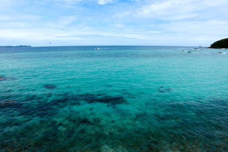 Landscape of rocky beach and sea with distant mountains and islands, blue sky.