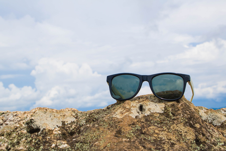 The old sunglasses , placed on the stone.The background is a mountain and the skyの写真素材