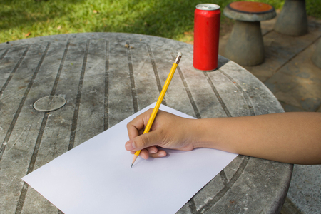 hand of a female holding a Yellow Pencil with papers On desk in the gardenの写真素材