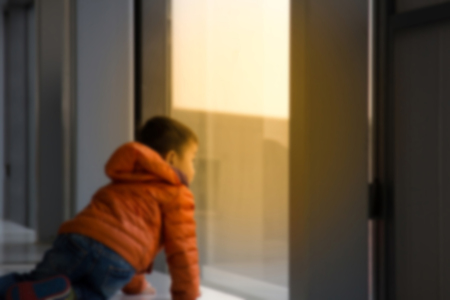 Abstract blur Rear view Little boy looking out the window In the room, abstract blur backgroundの写真素材