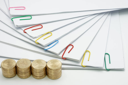 Pile of gold coins and pile of document with colorful paperclip on white background.
