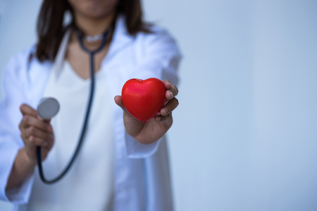 Closeup of young woman doctor hands with ball heart shape red on white background.の写真素材