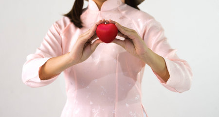 Closeup of young woman in pink dress hands with ball heart shape on white background.