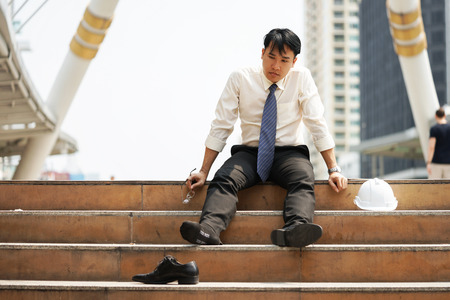 Businessman who are tired or stressed sit on the stairs after working on the building background.の写真素材