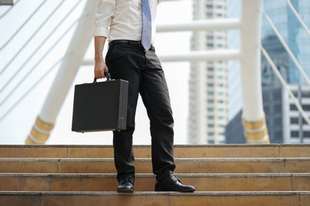 Businessman stand alone holding document bag at ladder after working on modern walkway with a building background.の写真素材