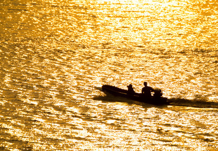 Silhouette of a boatman in river on golden sunshine background.の写真素材