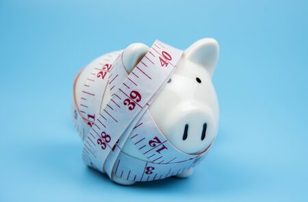 Piggy bank with measuring tape isolated on blue pastel background,healthy or over weight conceptの写真素材
