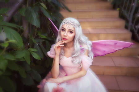 Young attractive girl dressed as fairy in green garden with pink wingsの写真素材