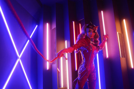 Sexy young woman in leather red dress with cat mask in neon lights with the whipの写真素材