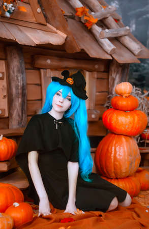 Pretty young girl witch halloween costume portrait dressed in black with pumpkinsの写真素材
