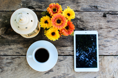 a cup of coffee and tablet on wood floor with flowerの写真素材