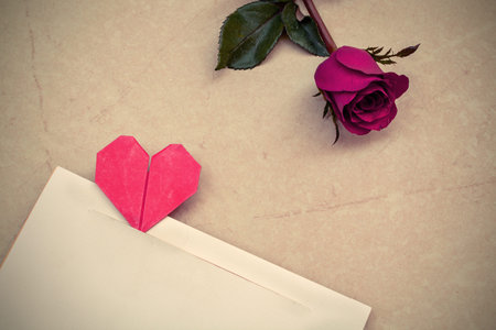 Red rose and petals with heart shape paper on stone background