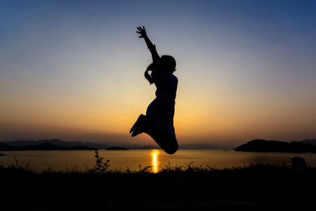 Silhouette of a girl jumping over sunsetの写真素材