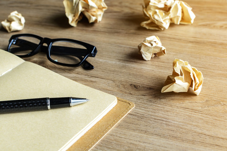 Crumpled paper balls with eye glasses and notebook on wood desk with soft lightの写真素材