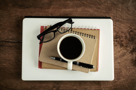 Laptop with notebook and cup of coffee on old wooden table, Vintage toneの写真素材