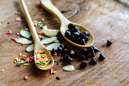 Chocolate chips on wooden spoon and ingredients for cooking dessertの写真素材