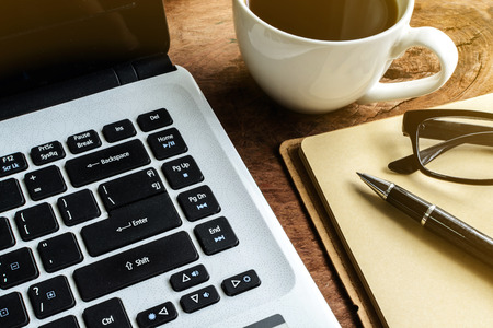 Laptop and cup of coffee on old wooden table with soft lightの写真素材